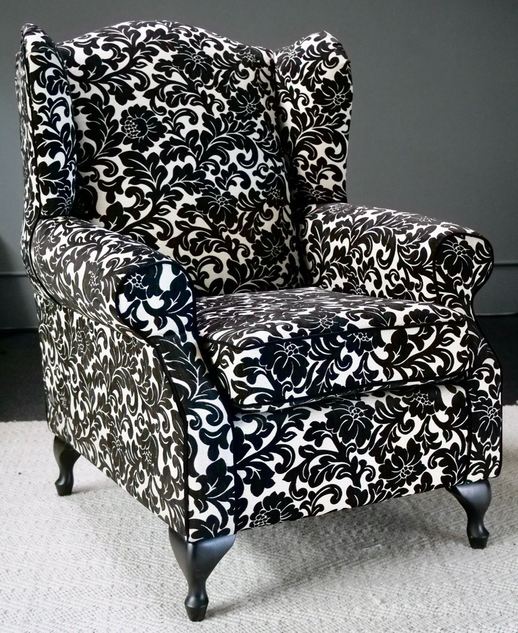 Wingback armchair in black and white floral pattern, set against a gray wall.