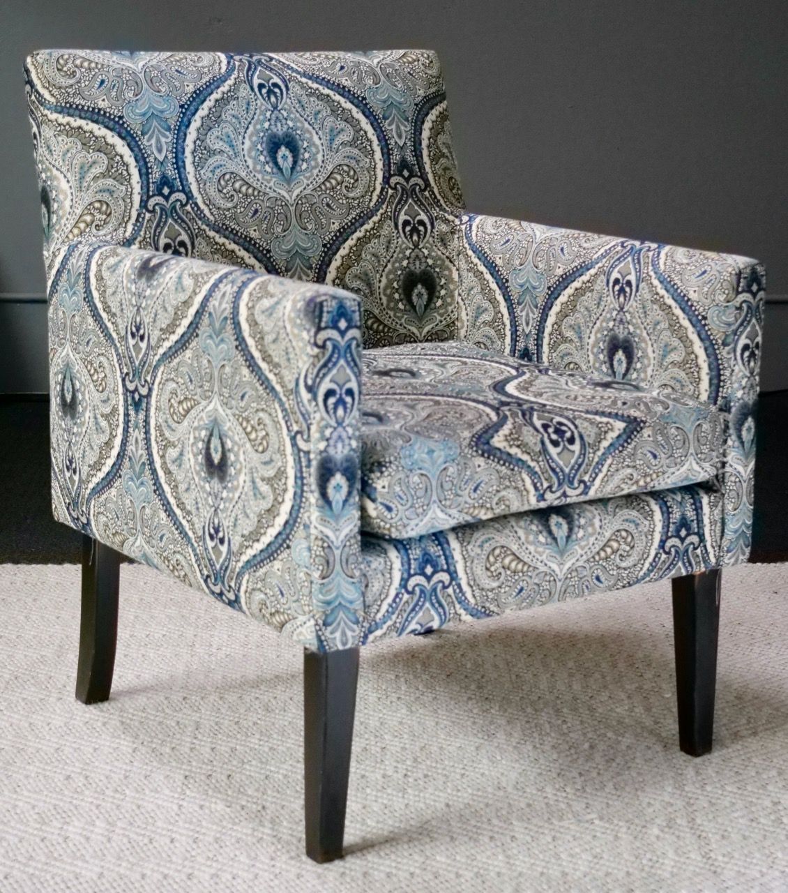 Upholstered armchair with a blue and gray paisley pattern, dark wood legs, on a light rug.