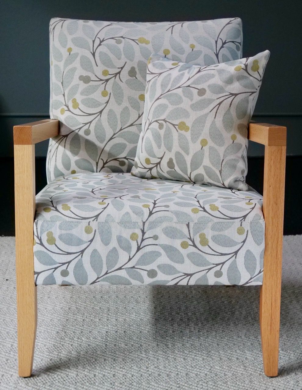 Armchair with light wood frame and floral patterned cushions, set against a dark wall.