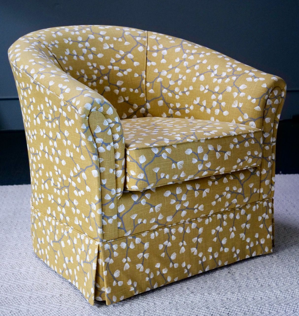 Yellow armchair with white floral pattern, on a light gray carpet.