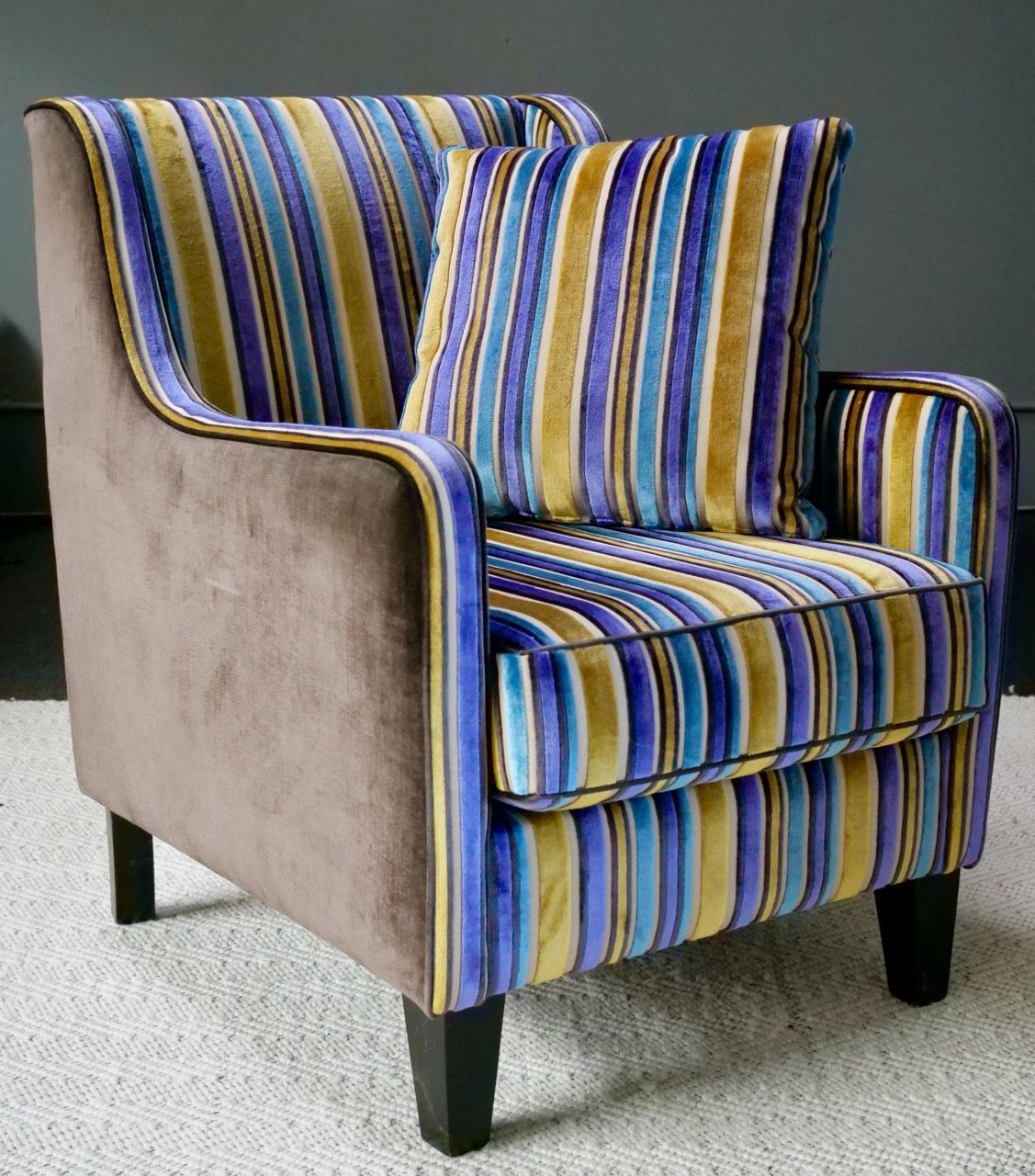 Armchair with colorful striped cushion and back, set against a dark wall.