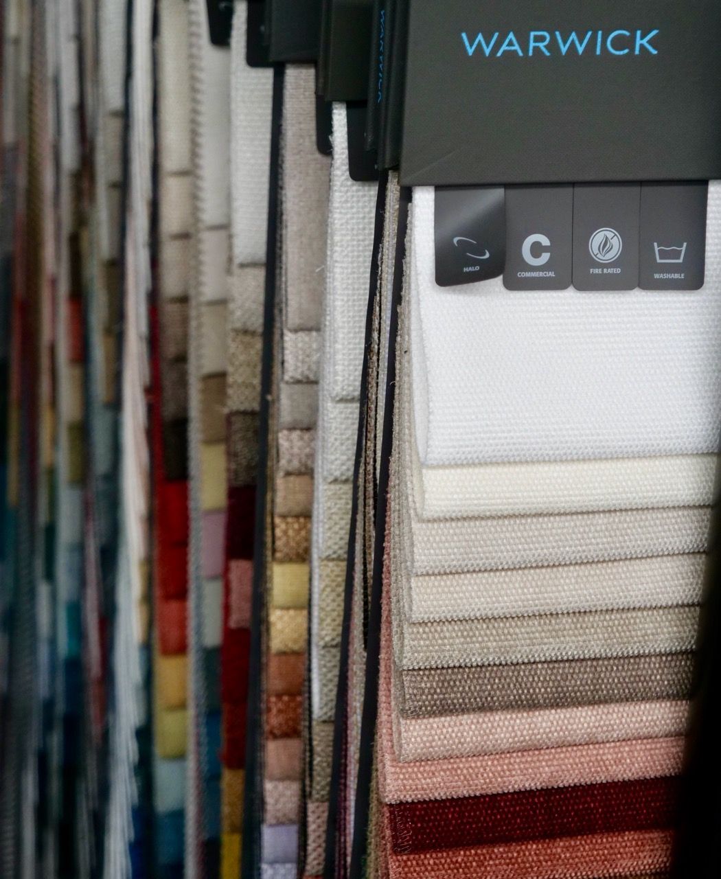 Fabric swatches in various colors hang from a display, Warwick brand visible.