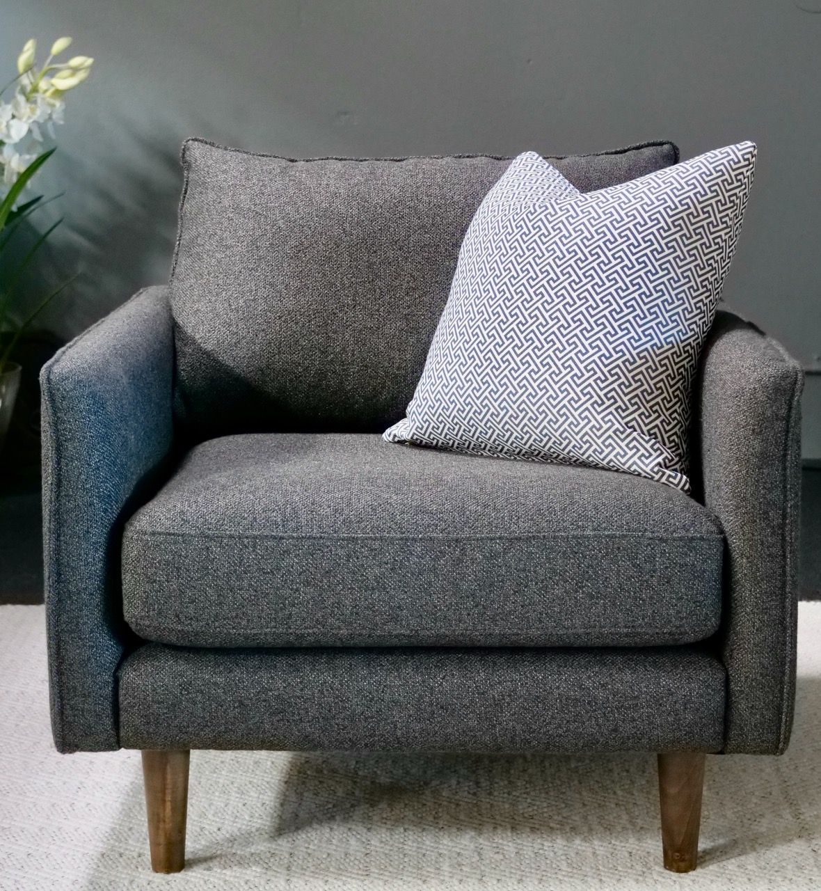 Gray armchair with gray and patterned pillows on a light rug, against a gray wall.