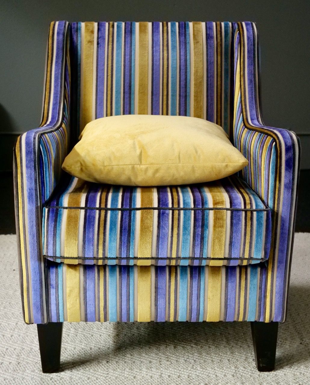 Armchair with blue, gold, and teal stripes, and a yellow pillow.
