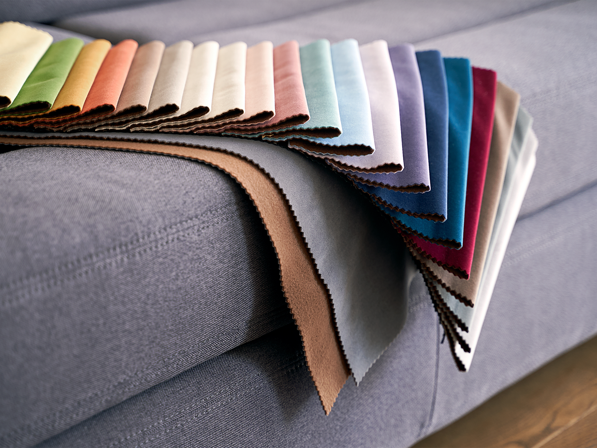 Fabric swatches fanned out on a gray sofa, showcasing various colors like beige, teal, and burgundy.