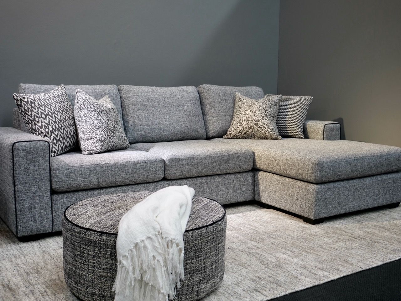 Gray sectional sofa with throw pillows and ottoman in a modern living room setting.
