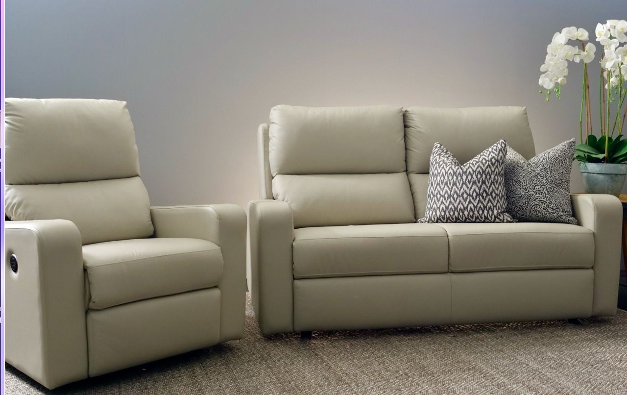 Cream-colored leather recliner chair and loveseat with two pillows; interior setting with white orchids.