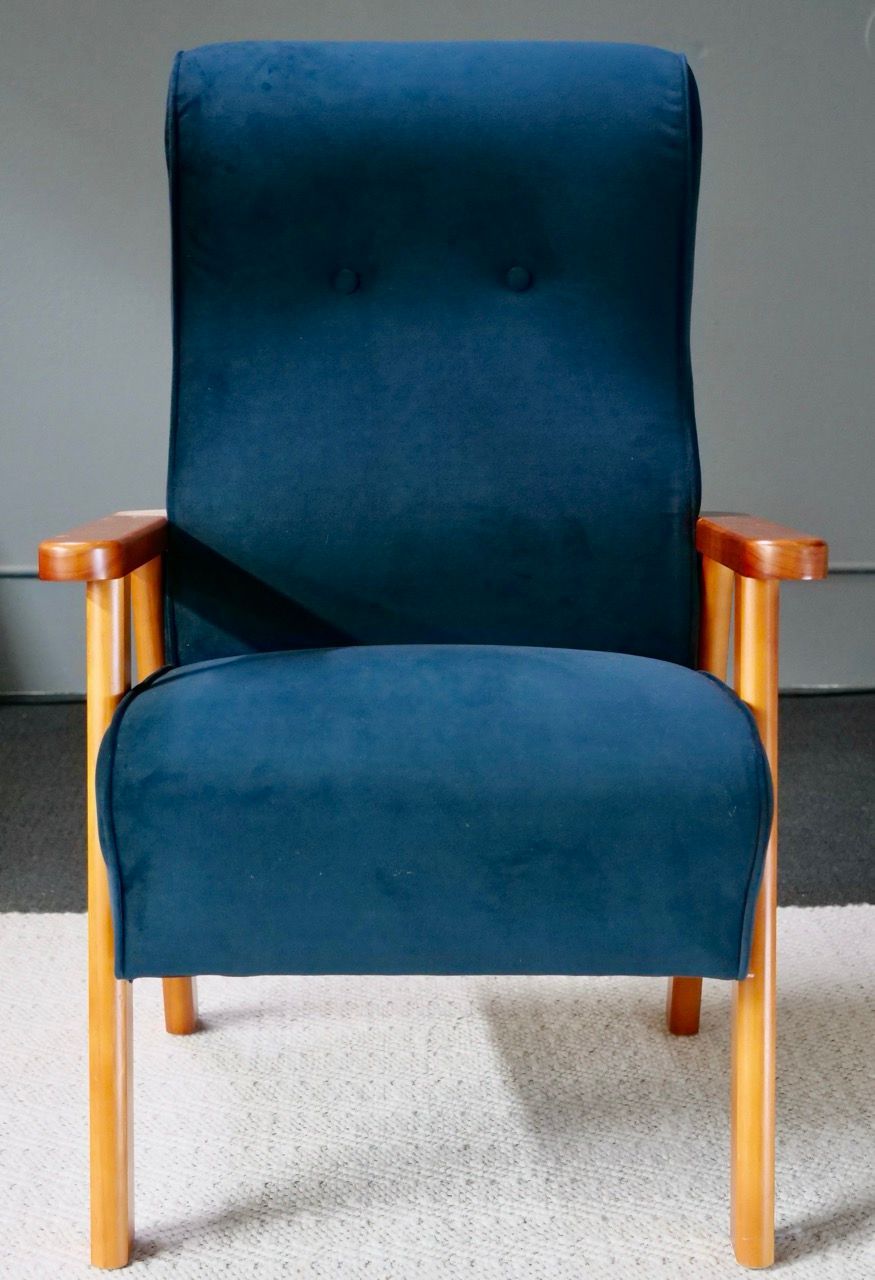 Blue upholstered armchair with wooden frame, against a gray wall.