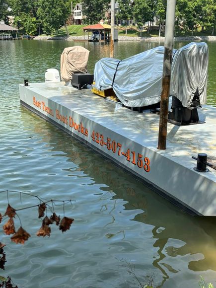 A boat dock on a lake with a covered watercraft parked on it and a phone number written on the side in orange text.