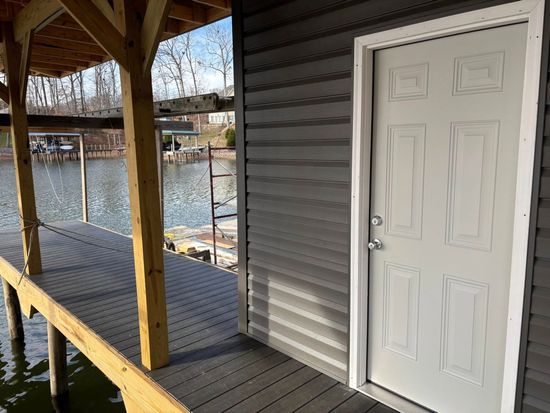 A light gray six-panel door on a dark gray siding wall, positioned on a wooden boat dock over a lake.