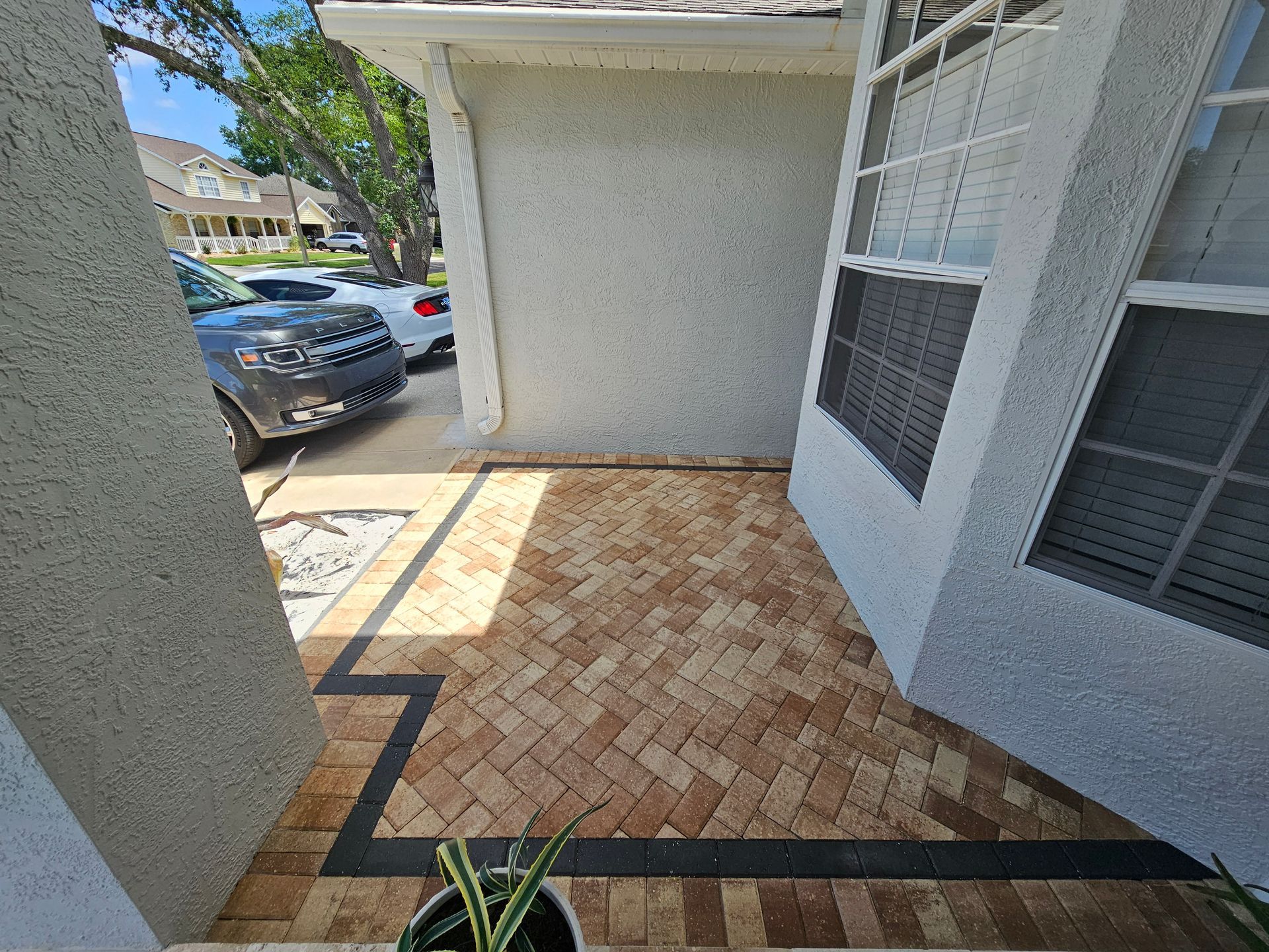 Entryway with brick pavers, black border, and window, with parked cars visible.