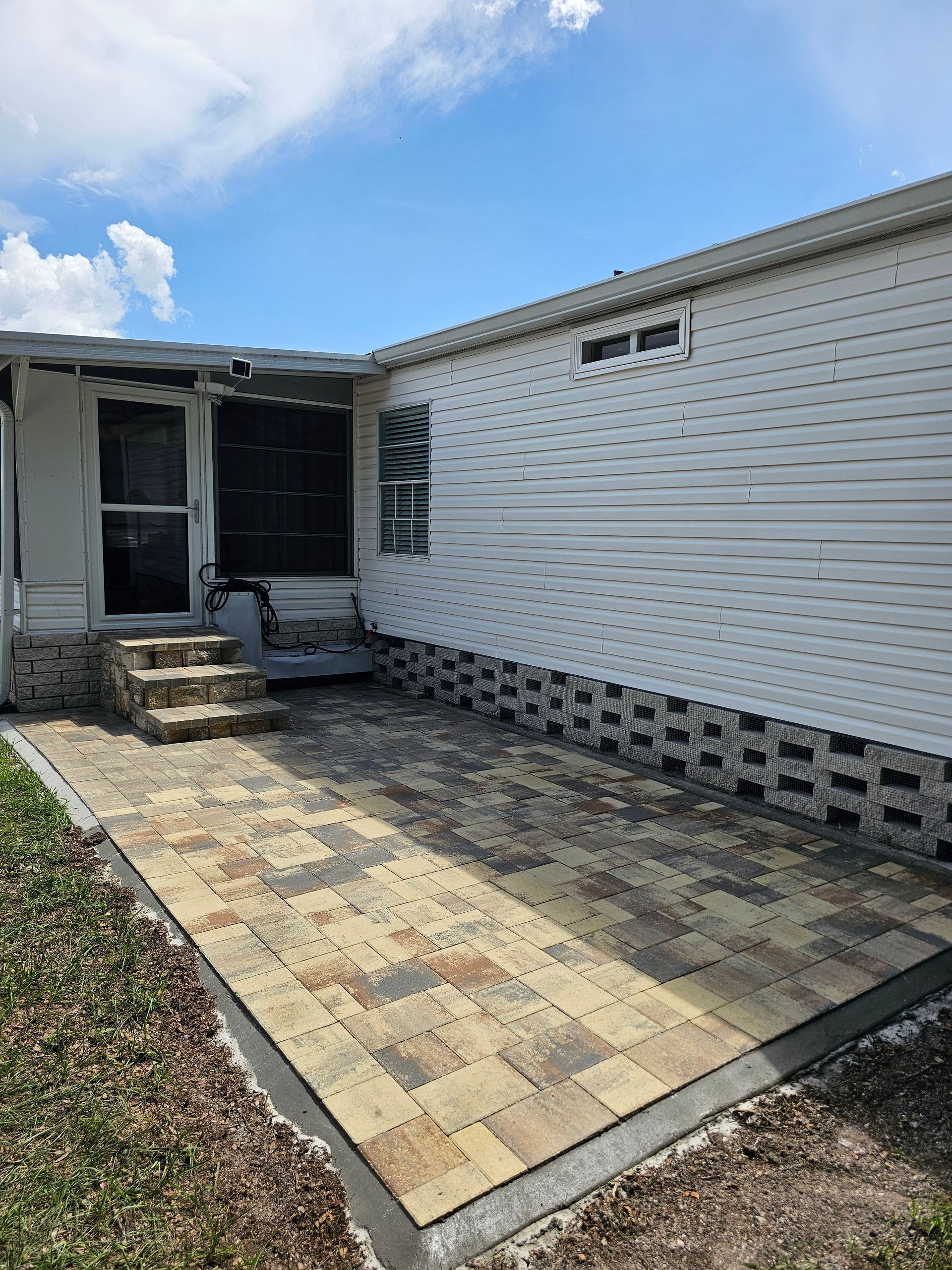 Brick patio next to a white house with a screened-in porch, under a bright blue sky.