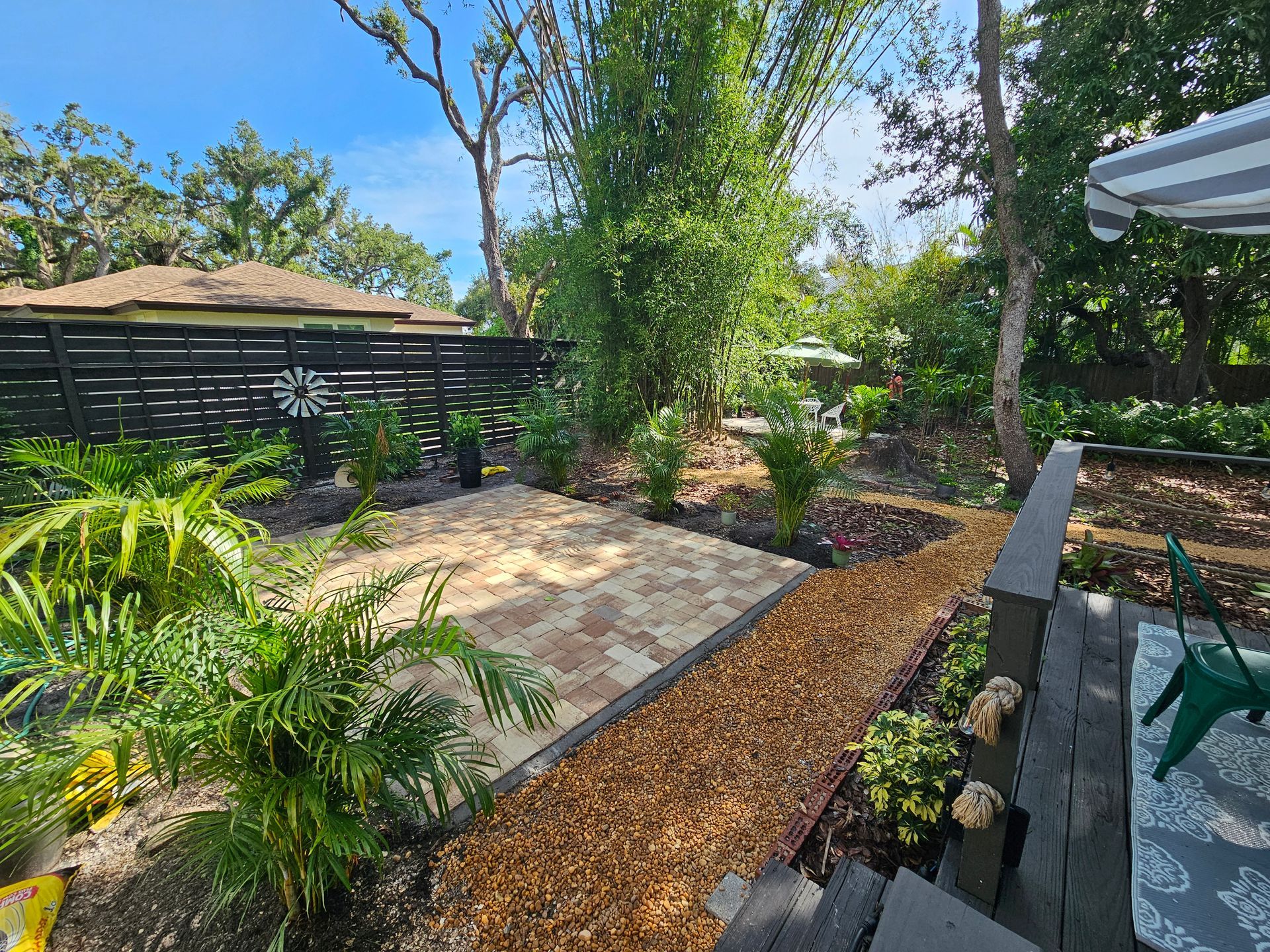 Backyard with patio, gravel path, plants, and black slatted fence.