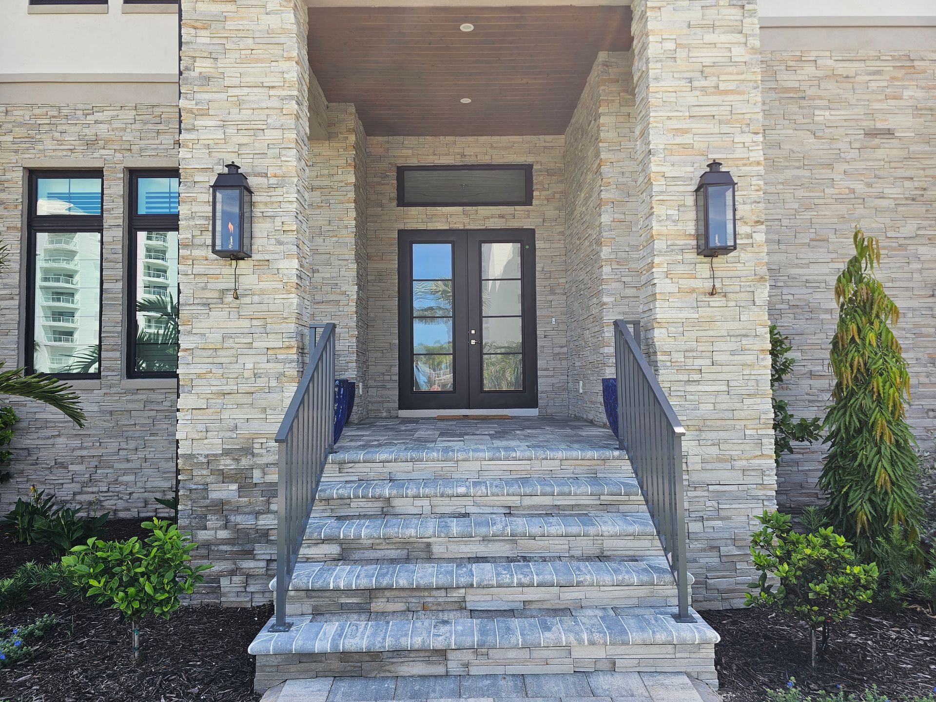 Stone facade entrance with steps, black double doors, lanterns, and blue planters.