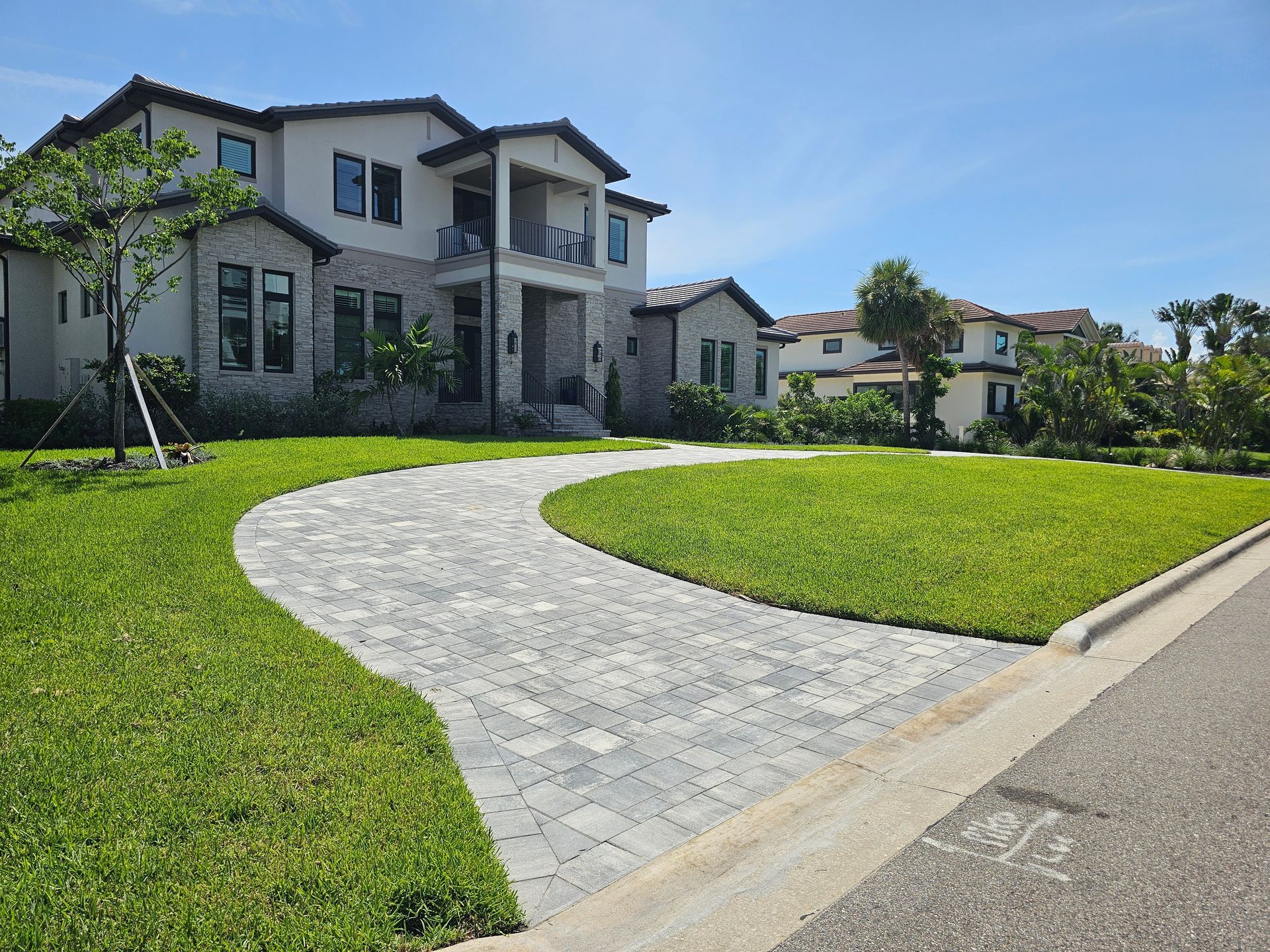 Two-story house with a curved paved driveway and green lawn, under a bright blue sky.
