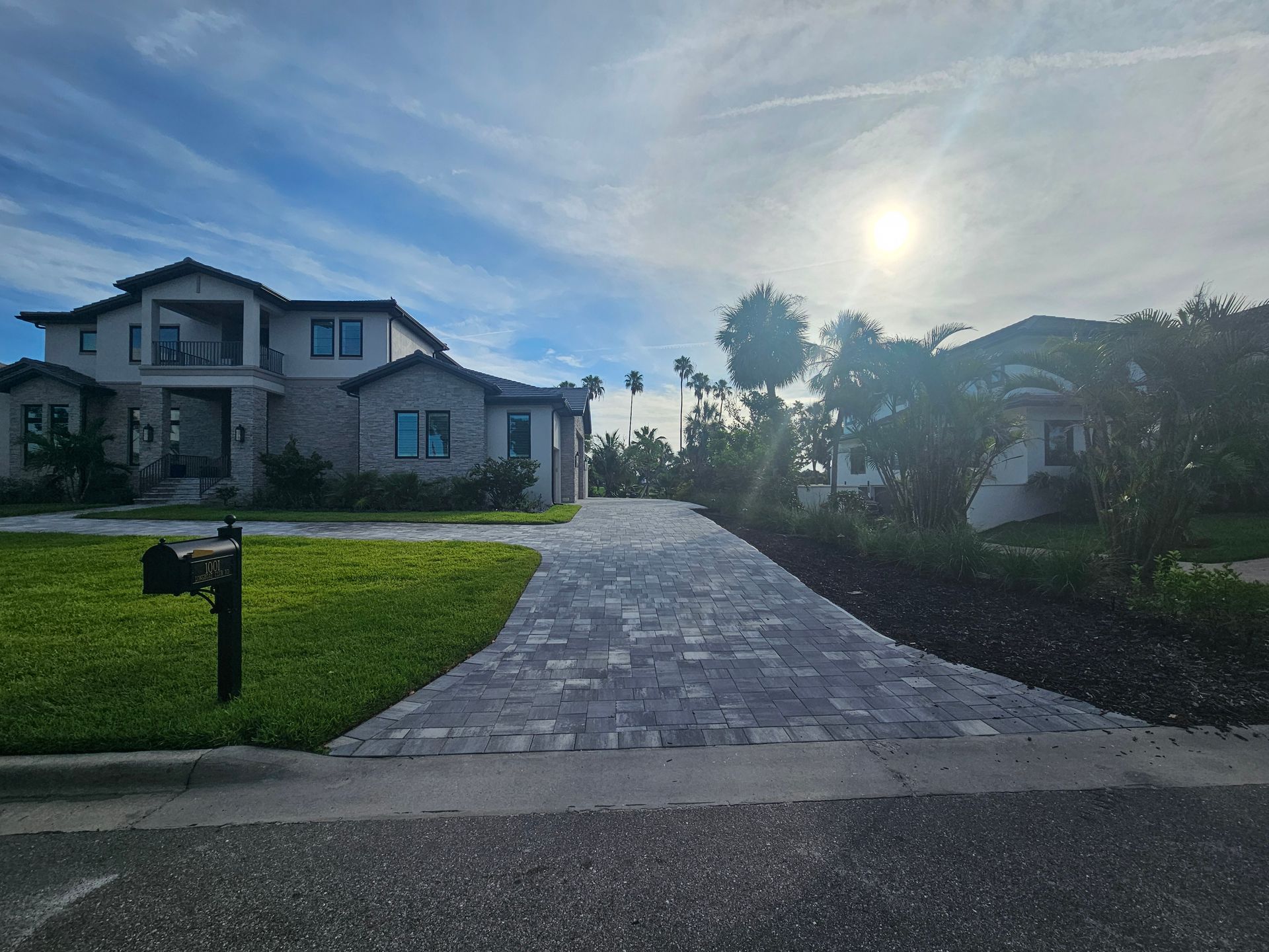 A two-story house with a brick driveway, mailbox, and green lawn on a sunny day.