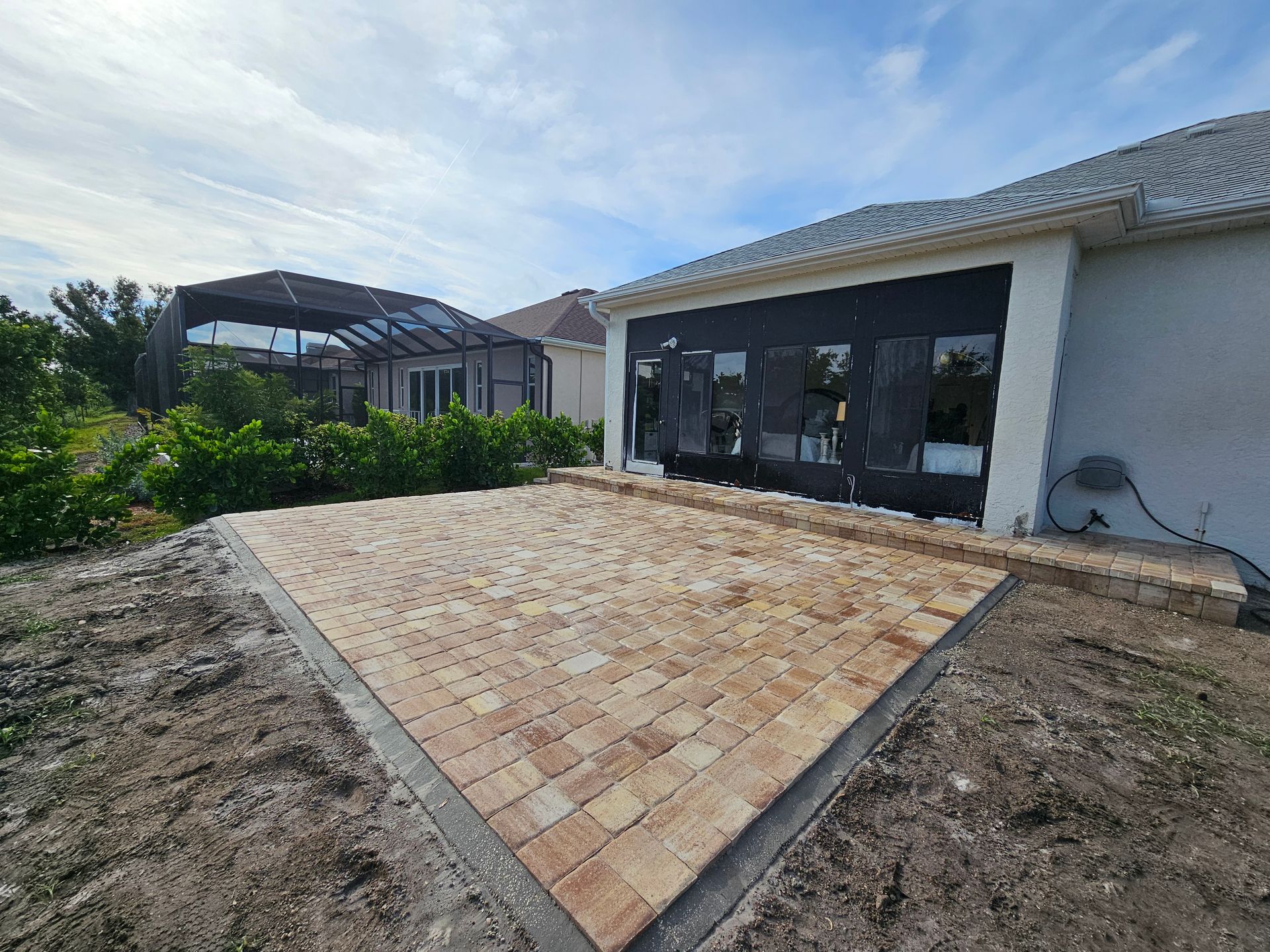 Brick patio outside a house with dark framed windows and a covered outdoor area.