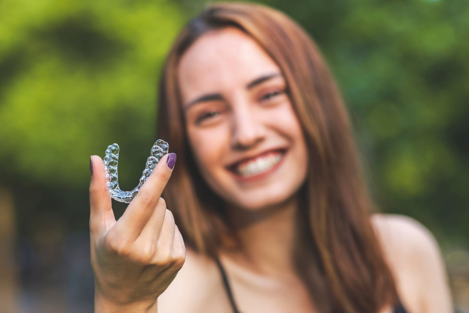 Photos of a woman holding a dental aligner while smiling.