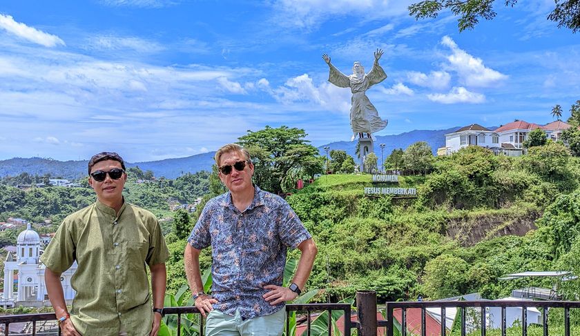 Two men are standing in front of a statue of jesus on a hill.