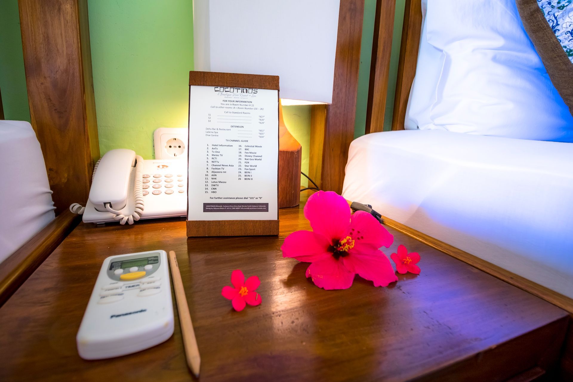 A hotel room with a remote control and flowers on the nightstand