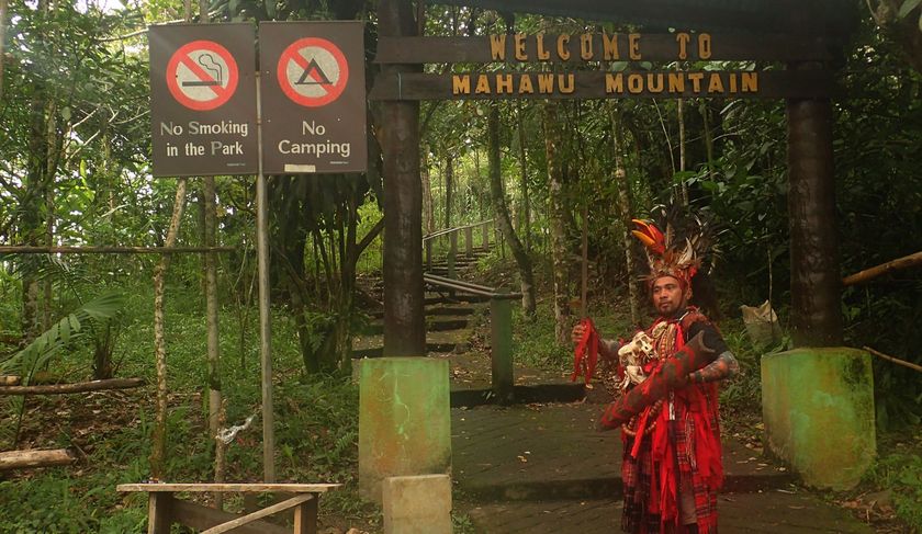 A man in a red costume is standing in front of a sign that says welcome to mahahu mountain