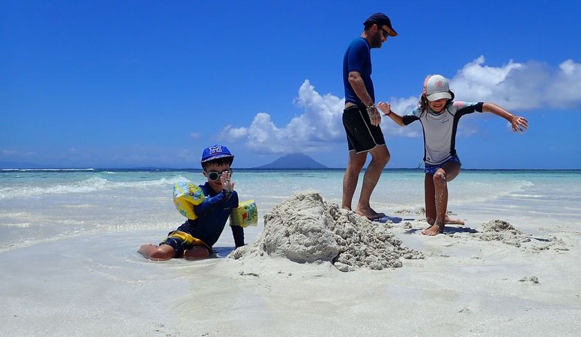 A man and two children are playing in the sand on the beach.
