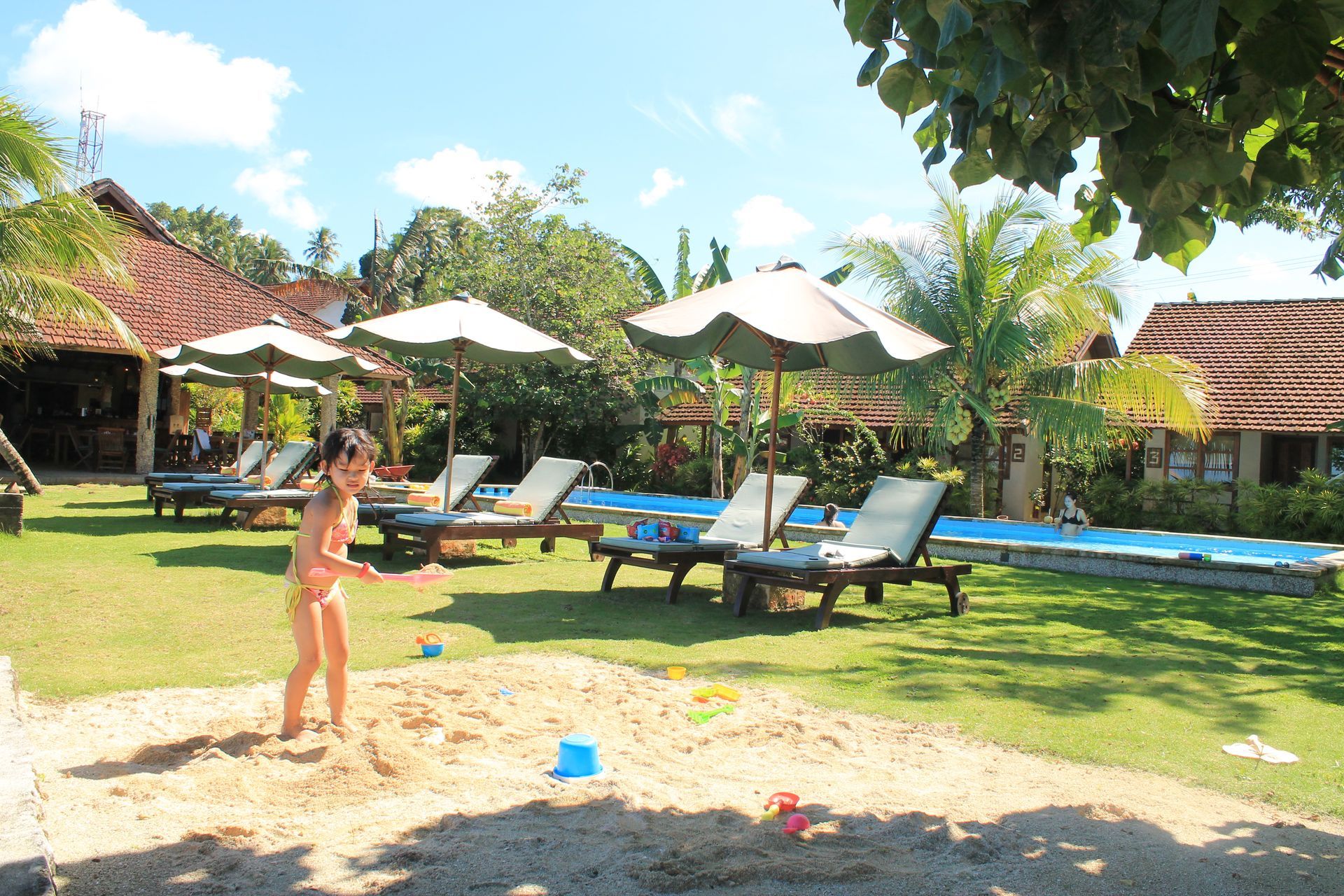 A girl in a bikini is playing in the sand near a pool