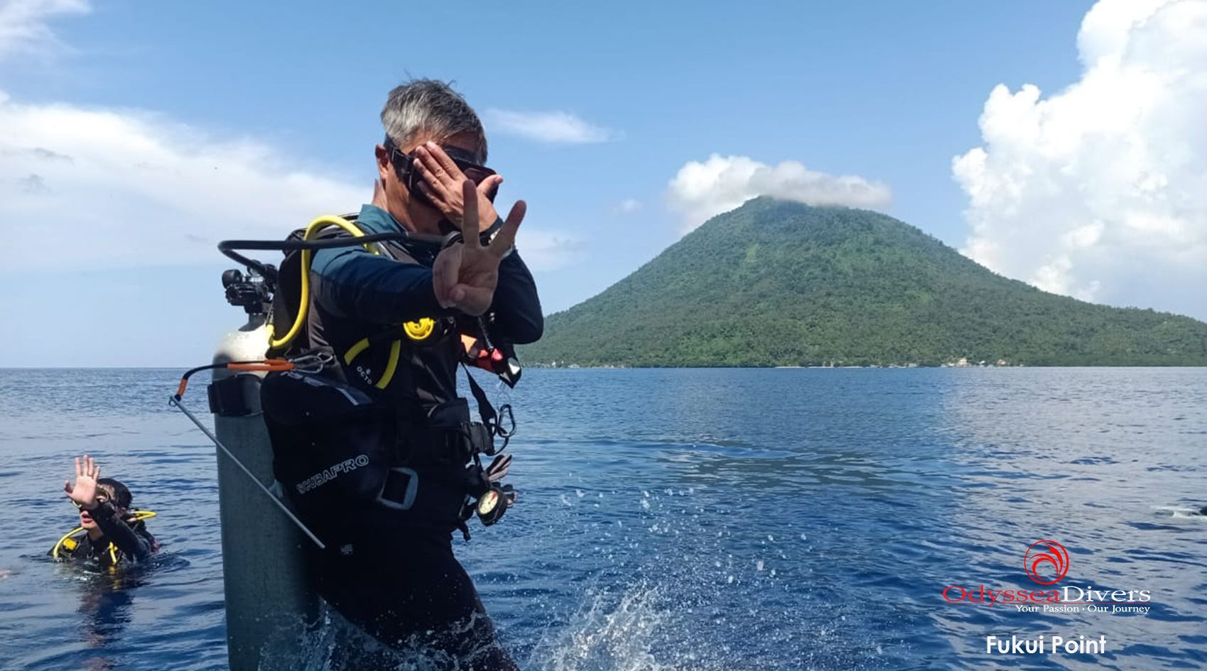 A scuba diver is standing in the ocean with a mountain in the background
