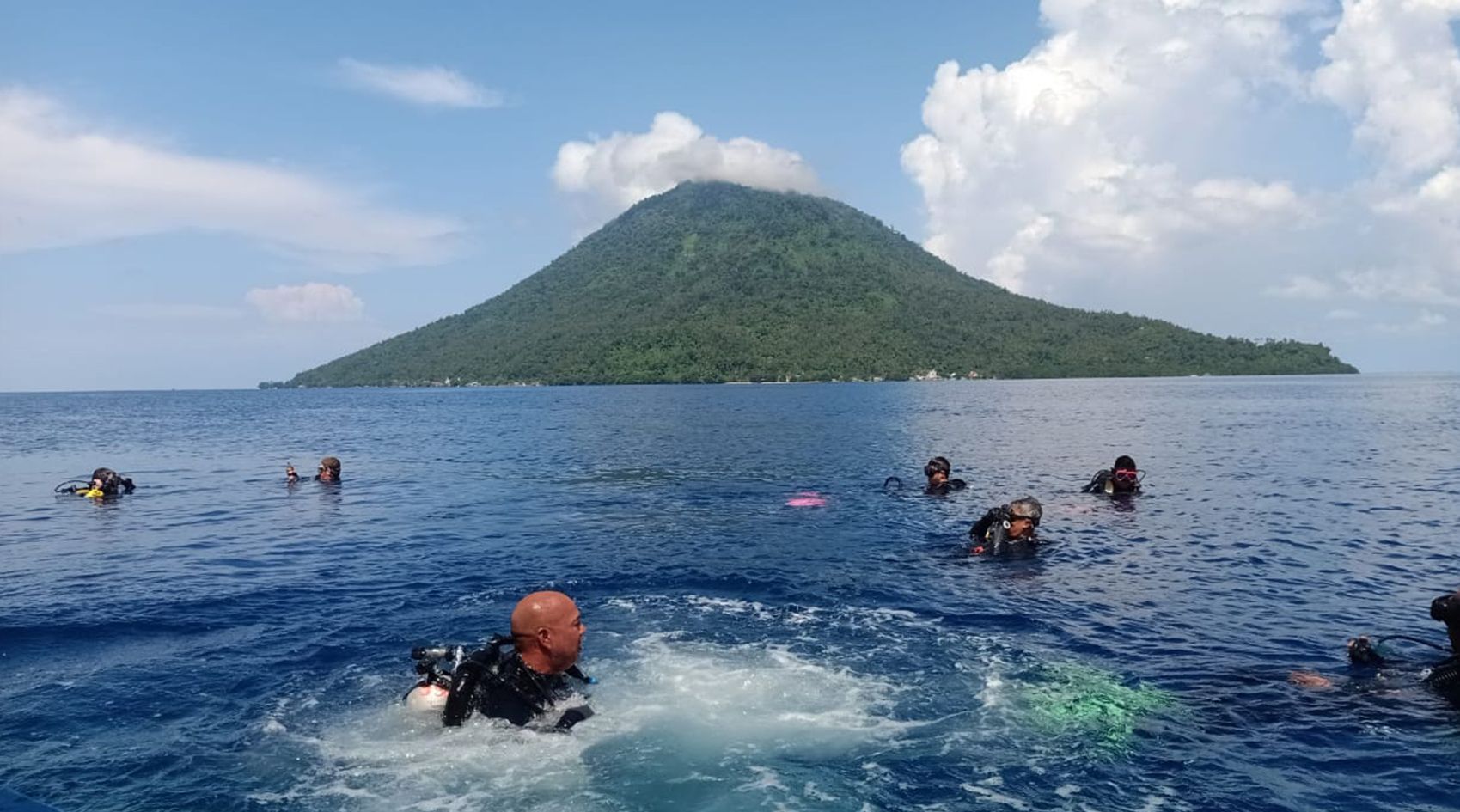 A group of people are swimming in the ocean with a mountain in the background.