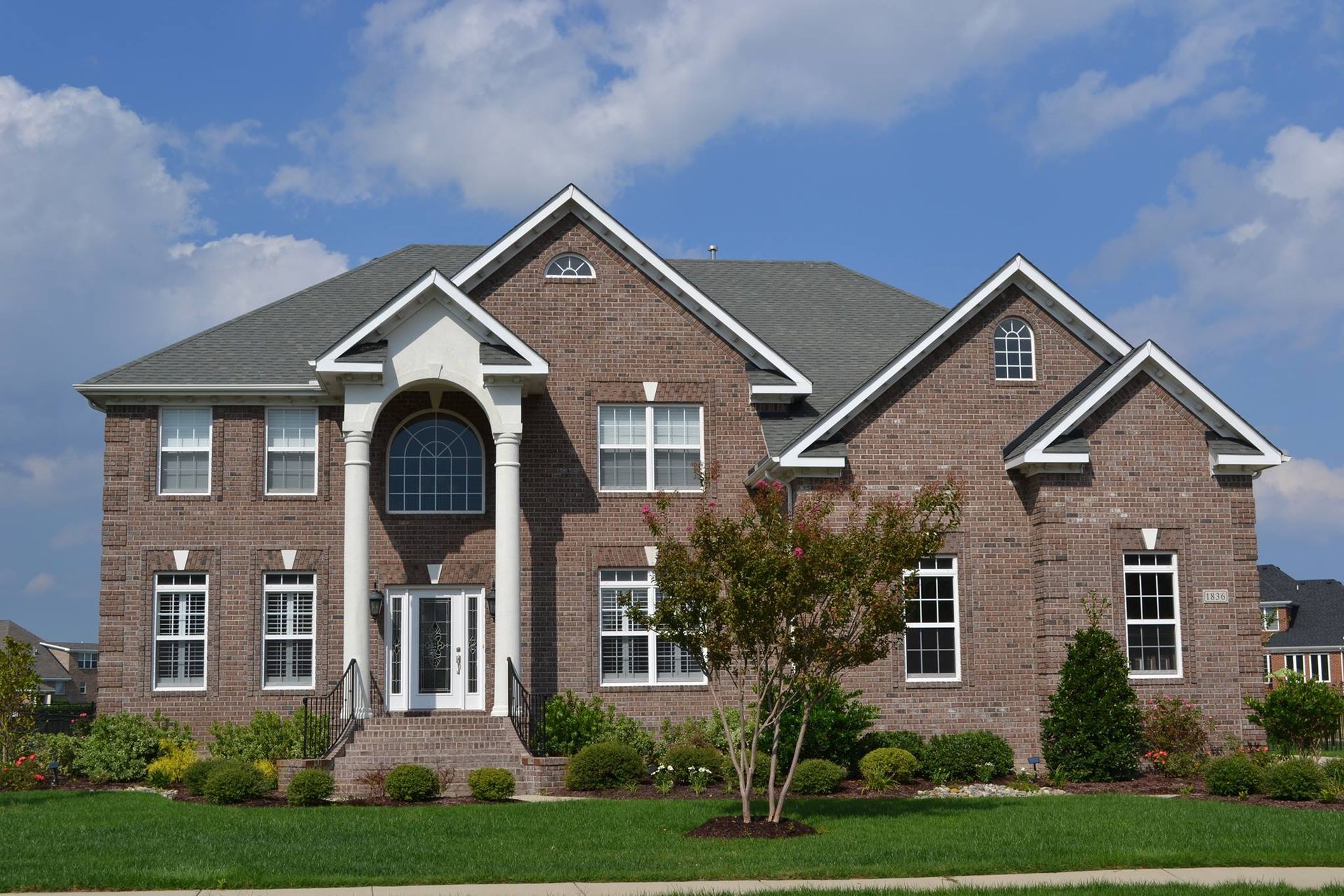 Two-story brick house with white trim, columns, and a landscaped yard under a blue sky.