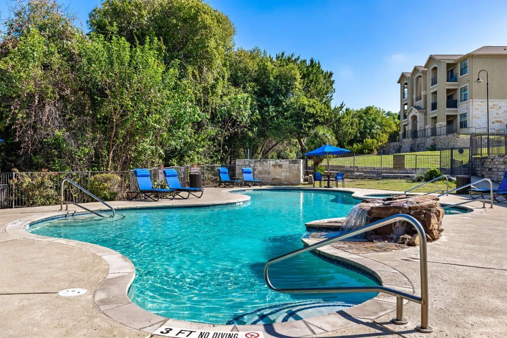 a large swimming pool with chairs and umbrellas in front of a building at Marquis at Canyon Ridge in Austin, TX