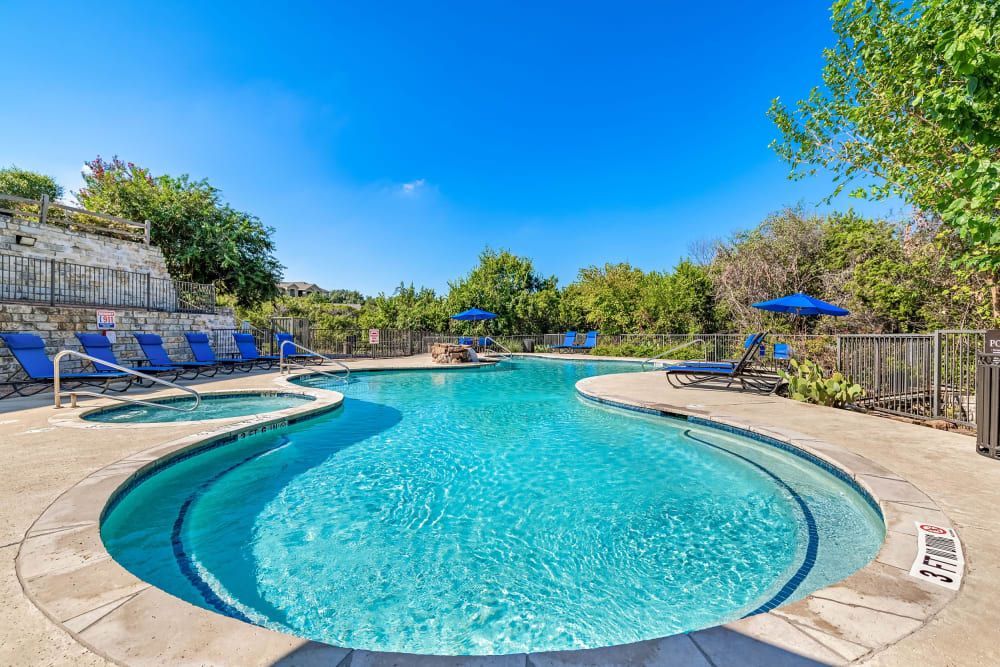 a large swimming pool surrounded by chairs and umbrellas on a sunny day at Marquis at Canyon Ridge in Austin, TX.