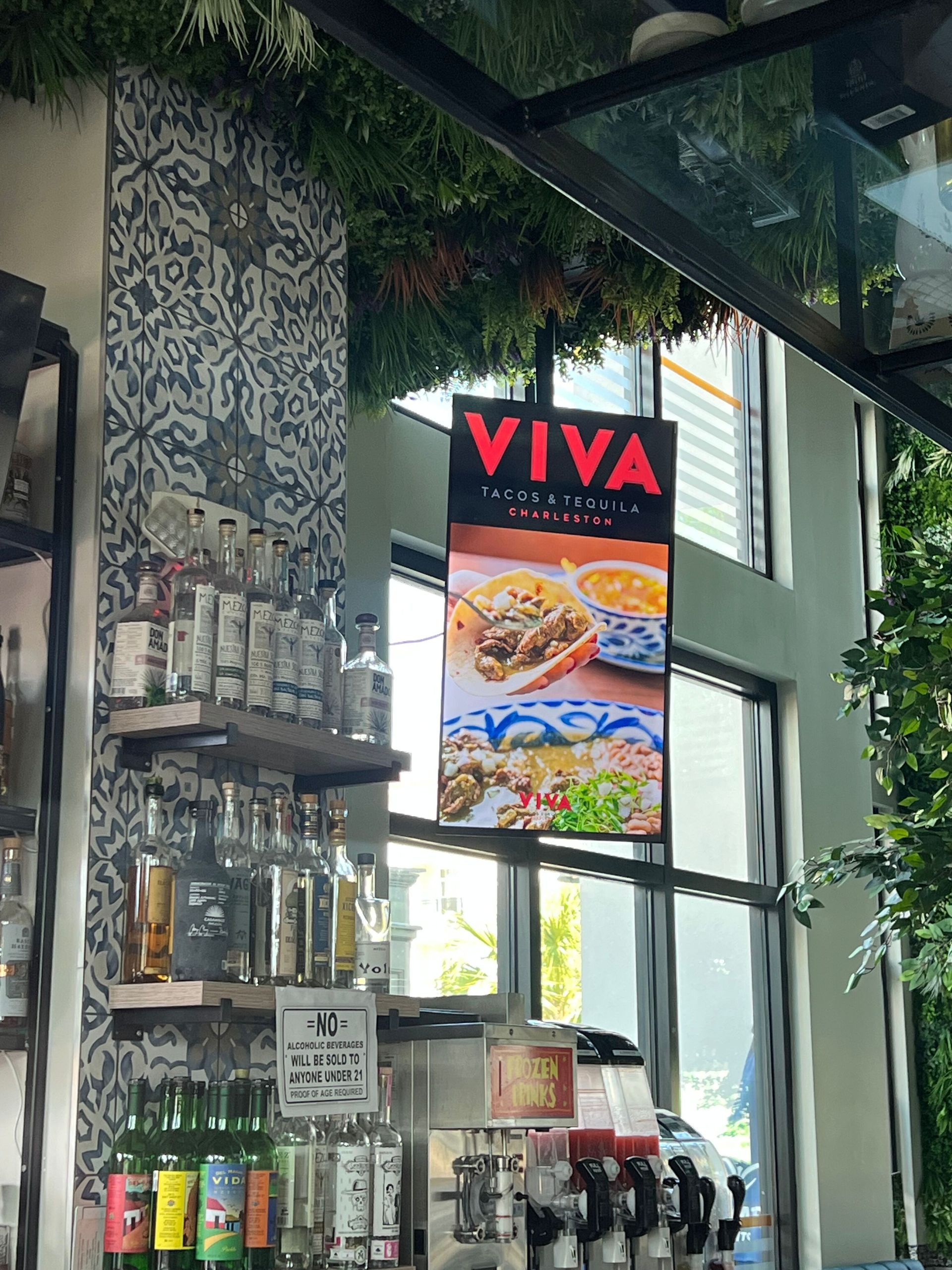 Viva restaurant sign hanging inside, near a bar with bottles and colorful decor. The sign displays images of food.