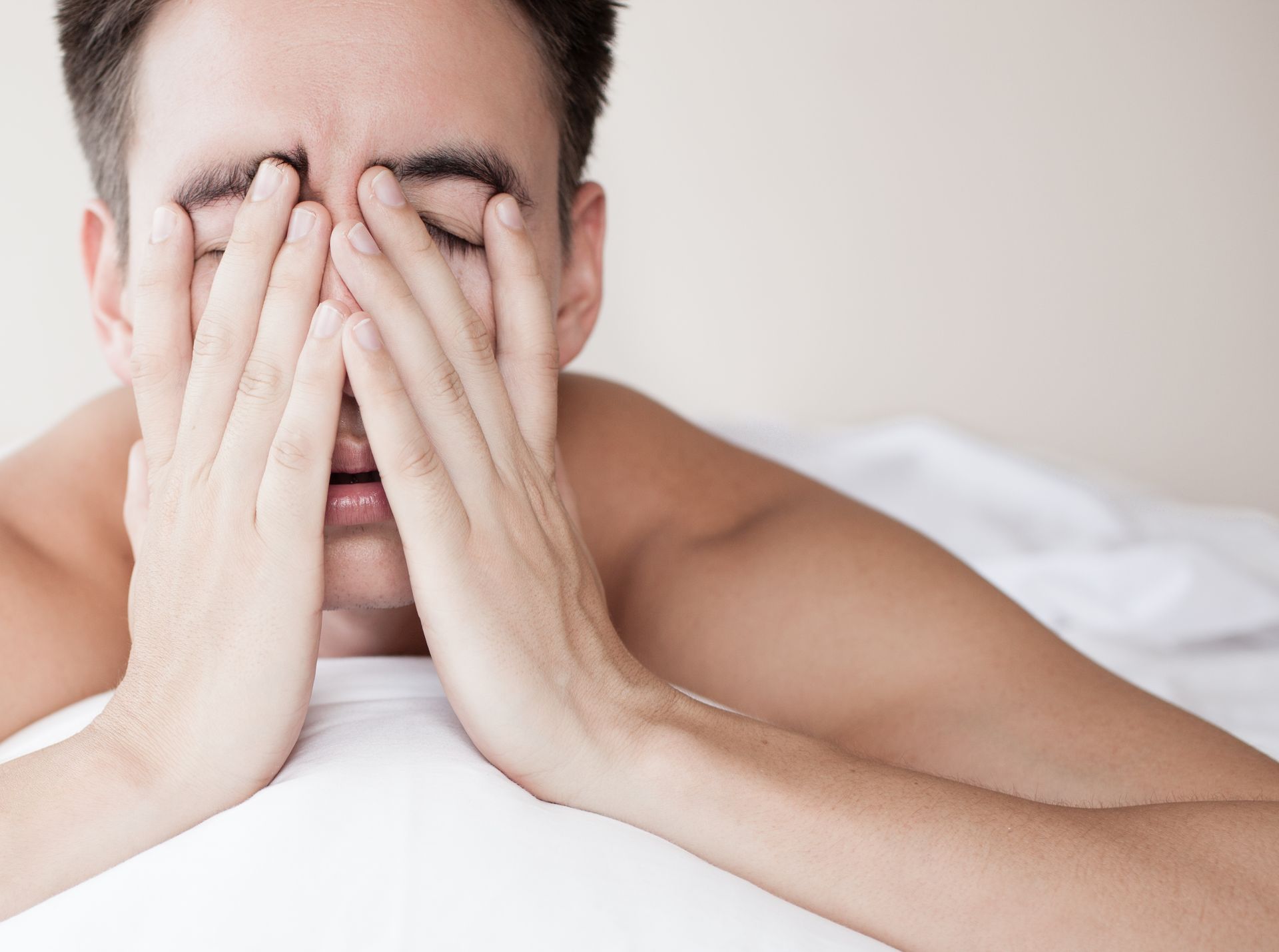A man is covering his face with his hands while laying on a bed.