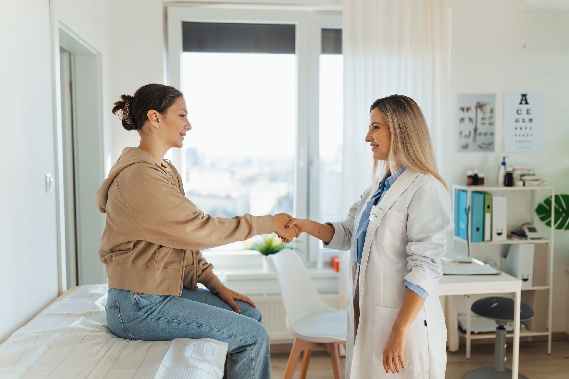 A woman is sitting on a bed shaking hands with a doctor.
