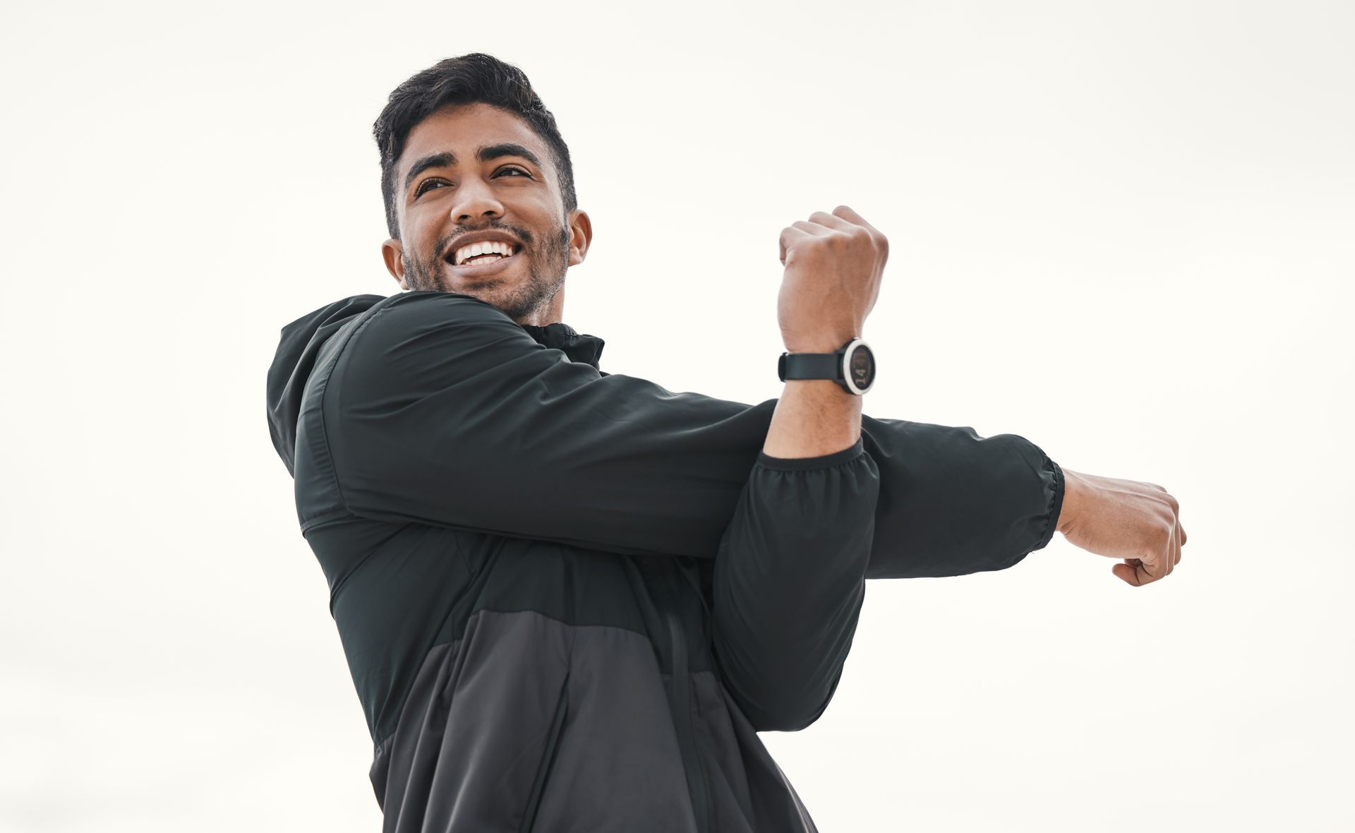 Man in black jacket stretching arm, smiling outdoors.
