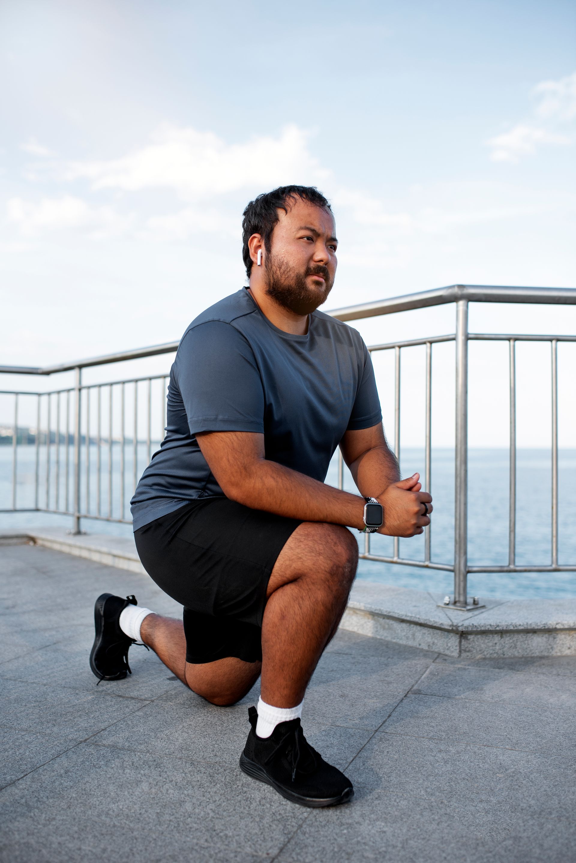A man is squatting on the ground near a railing.