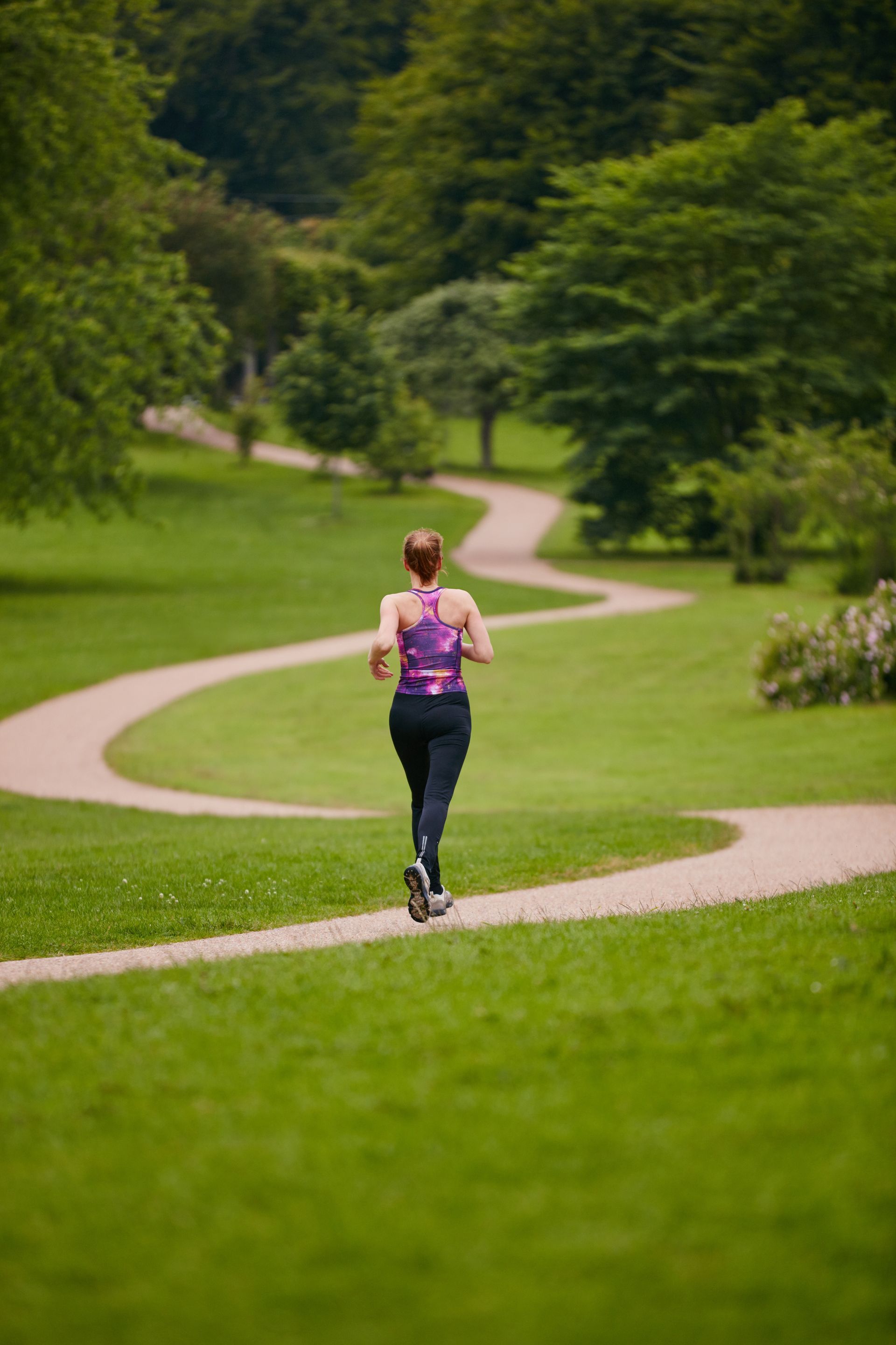 A woman is running down a path in a park.