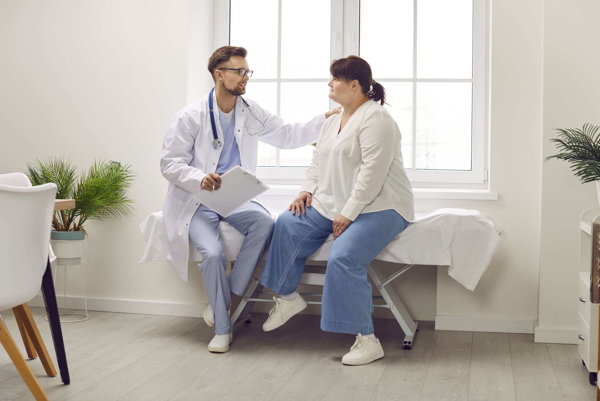 A doctor is talking to a patient who is sitting on a bed.