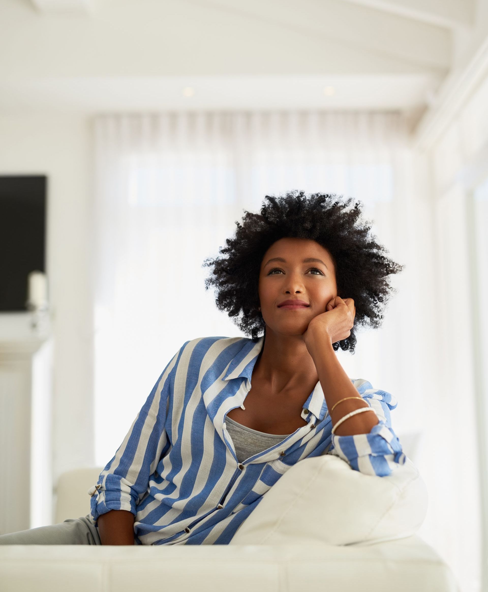 A woman in a blue and white striped shirt is sitting on a white couch.