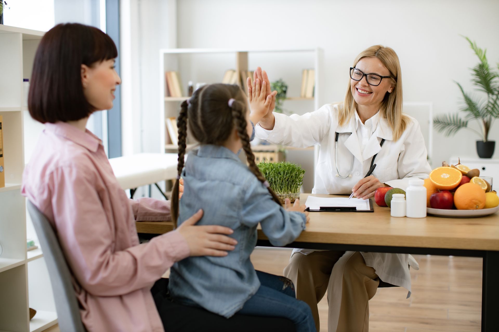 A woman and a little girl are giving each other a high five while sitting at a table.