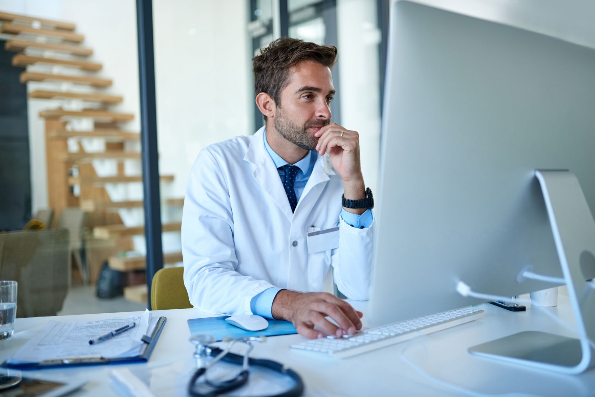 A doctor is sitting at a desk in front of a computer.