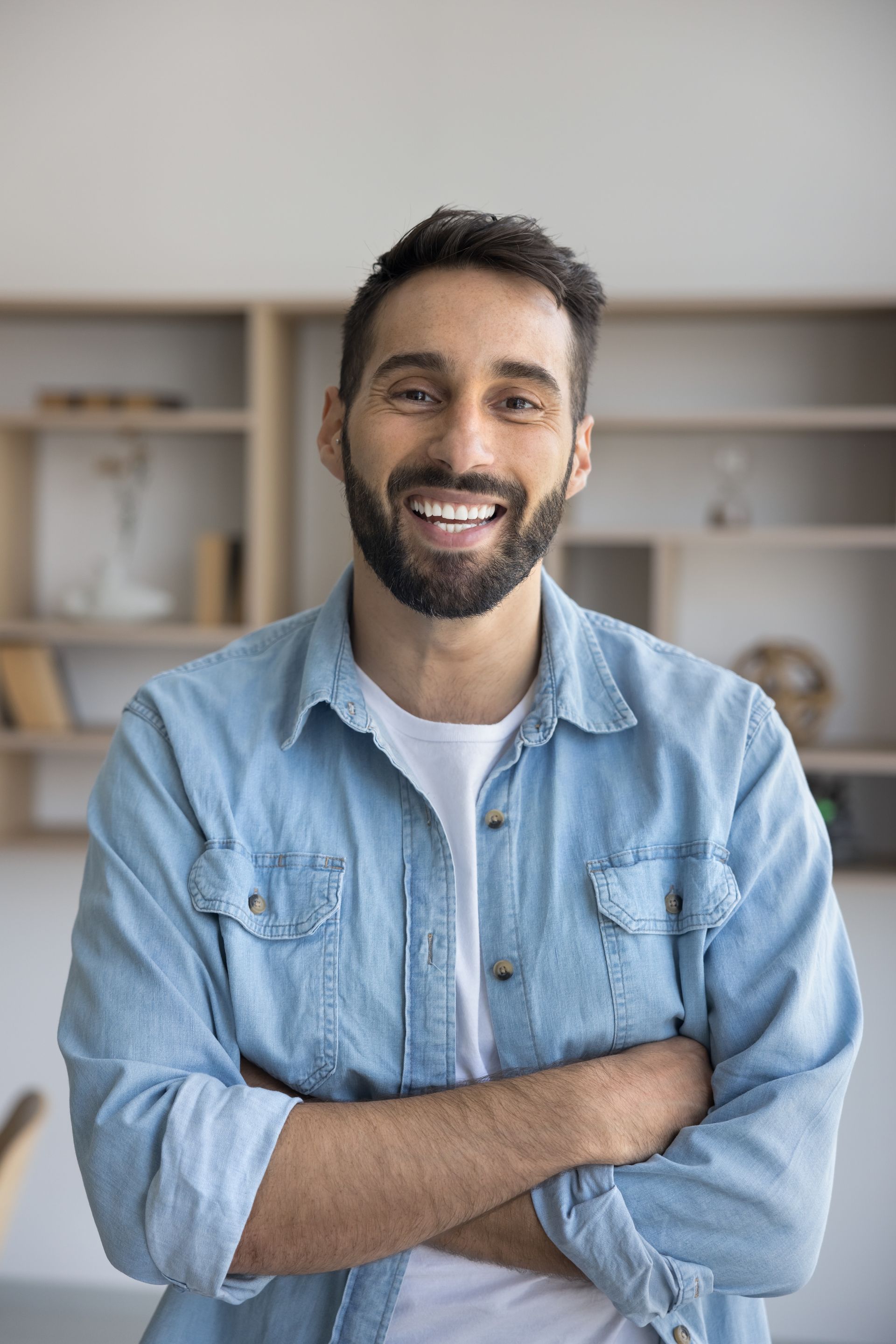 A man with a beard is standing with his arms crossed and smiling.