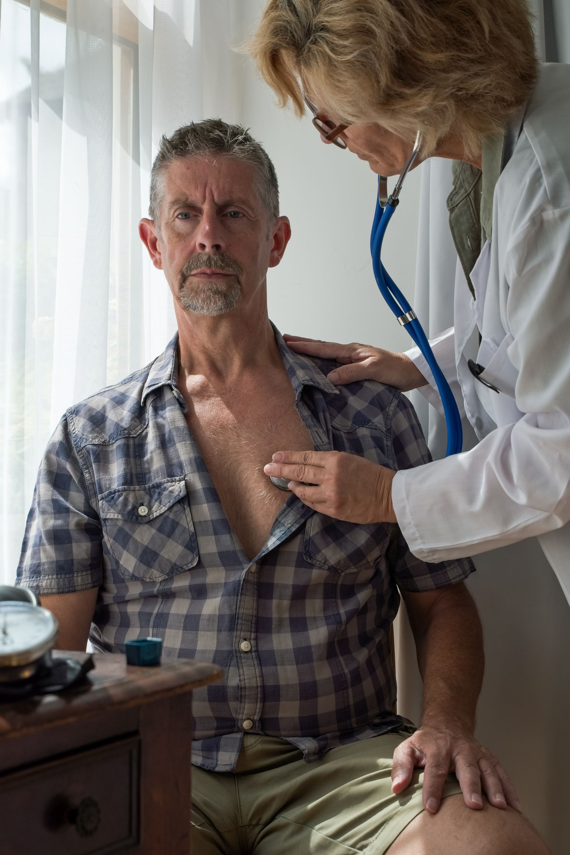 A doctor is listening to a man 's heart with a stethoscope.