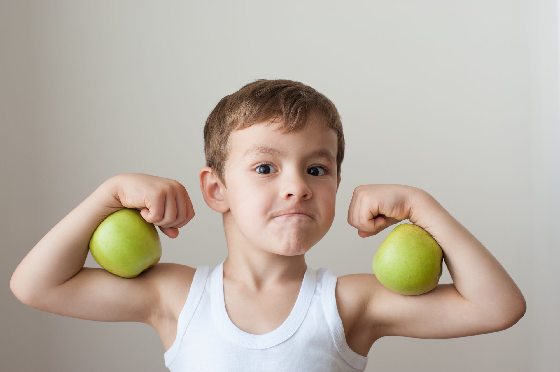 A young boy is flexing his muscles while holding two apples.