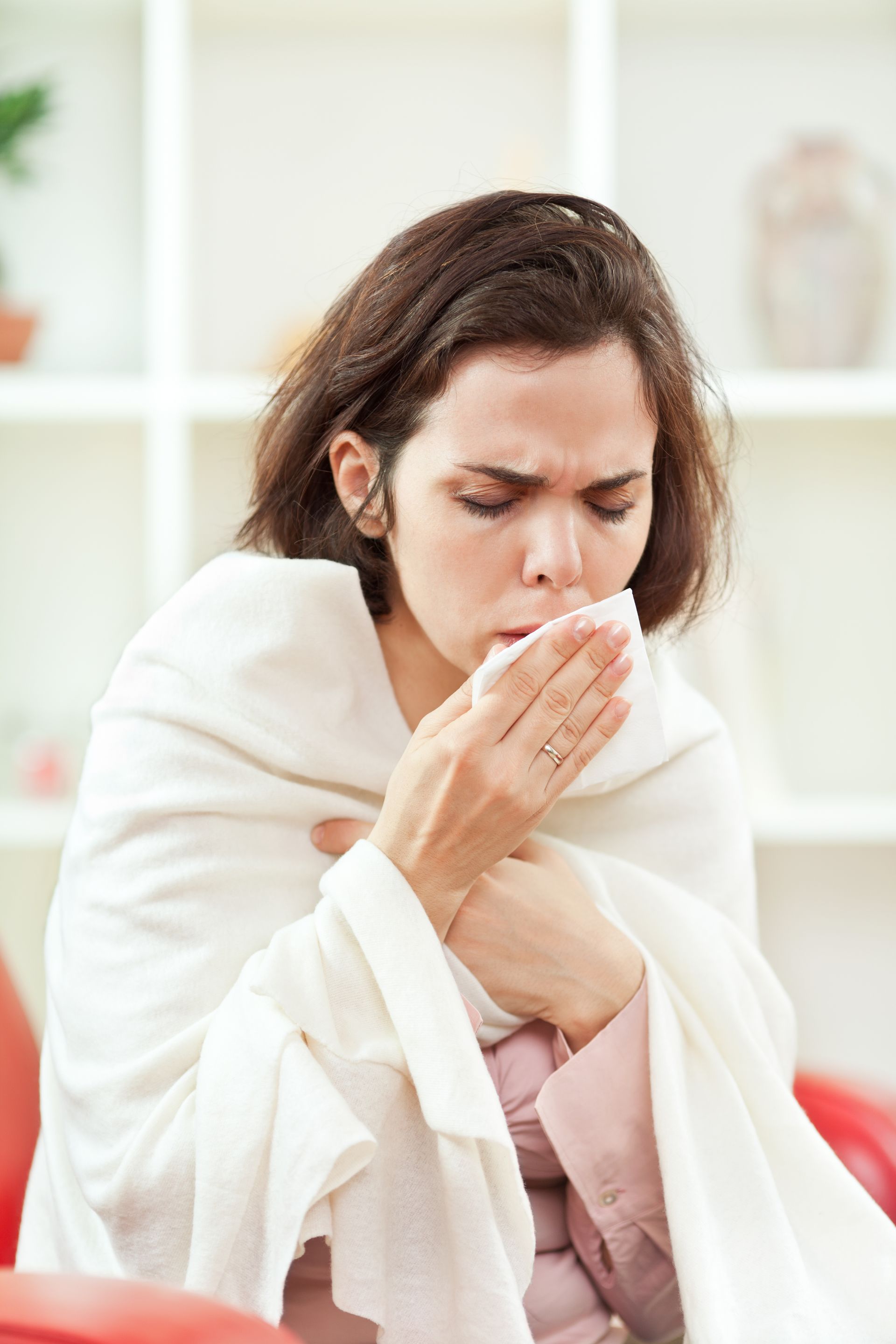 A woman wrapped in a blanket is blowing her nose into a napkin.