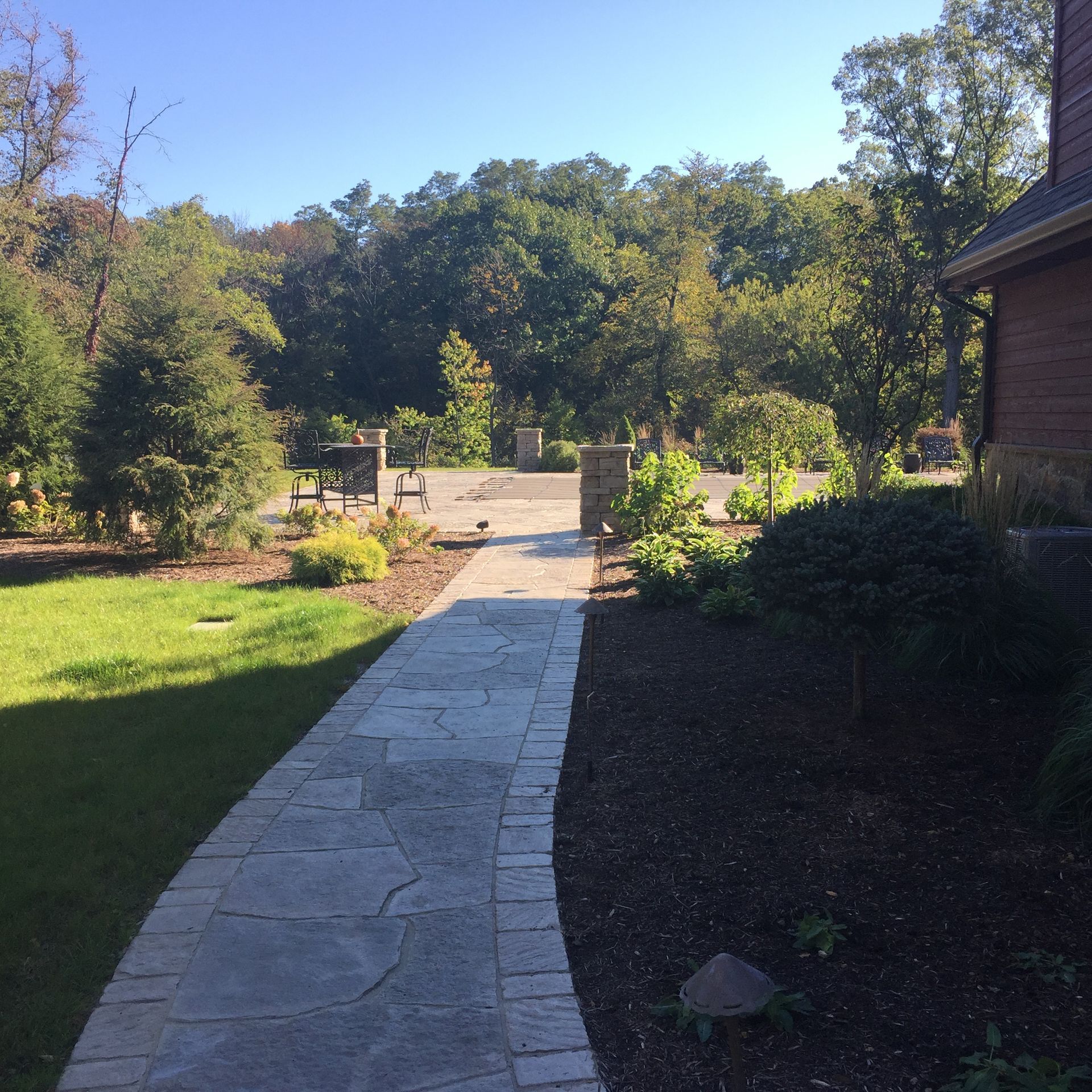 a stone walkway leading to a house with trees in the background