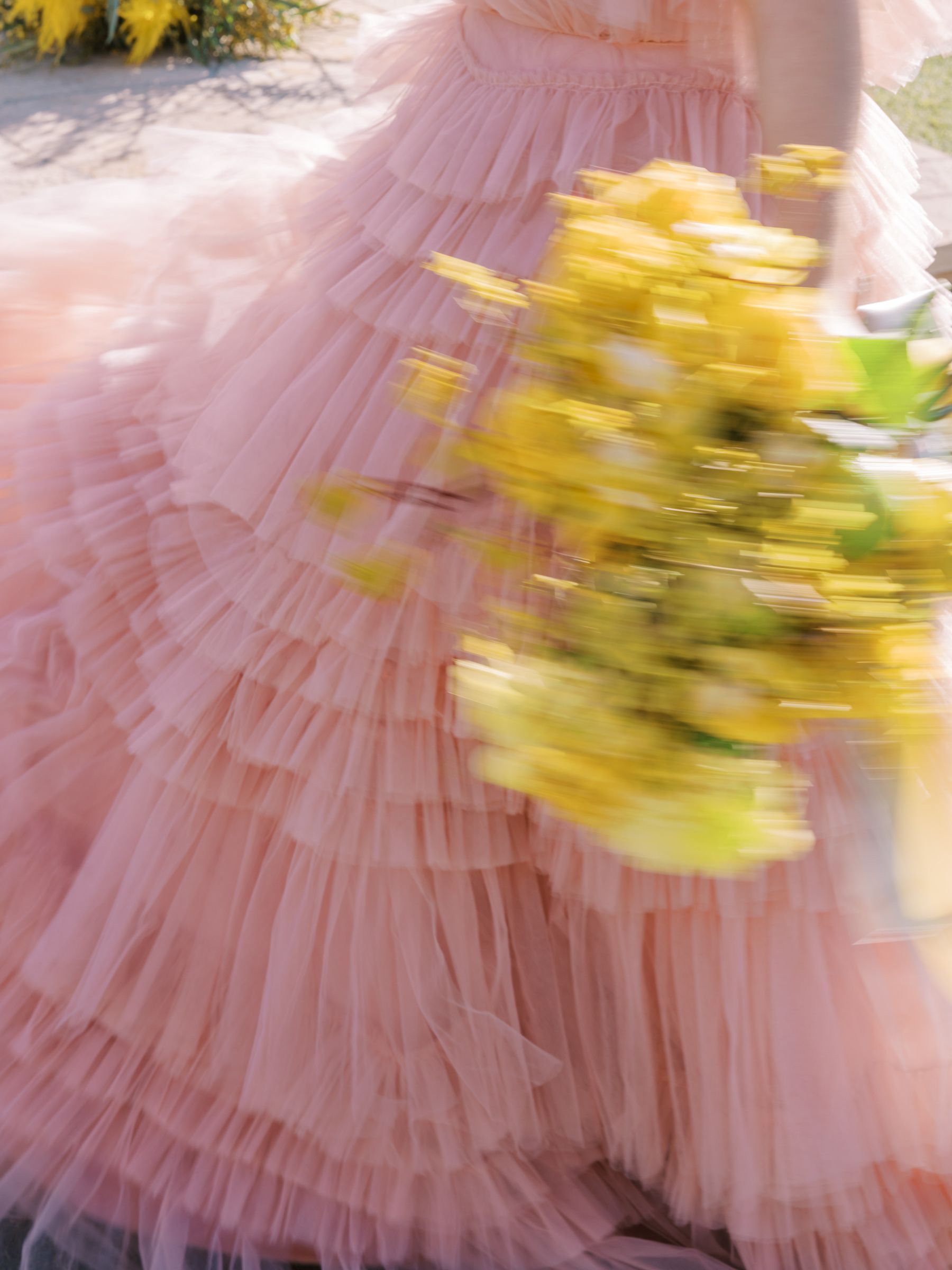 Two-tiered white wedding cake on silver stand, adorned with flowers, on a burgundy table, in front of a window.