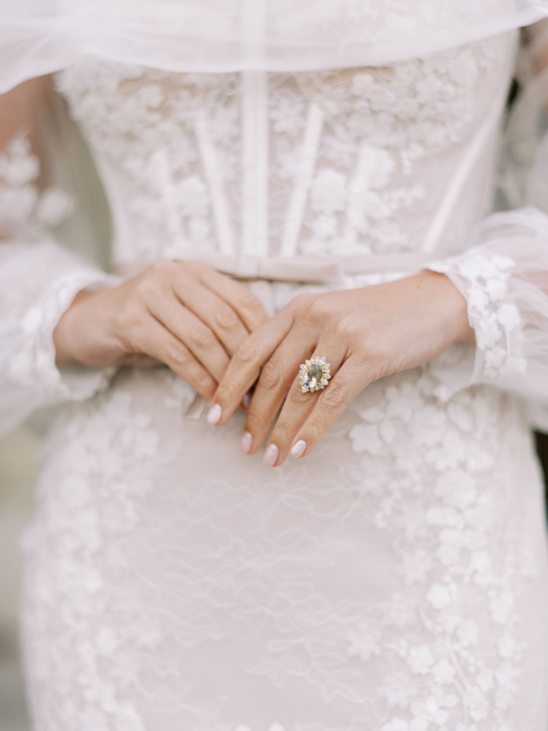 Bride's hands clasped, wearing a large, ornate ring, with a lace gown.