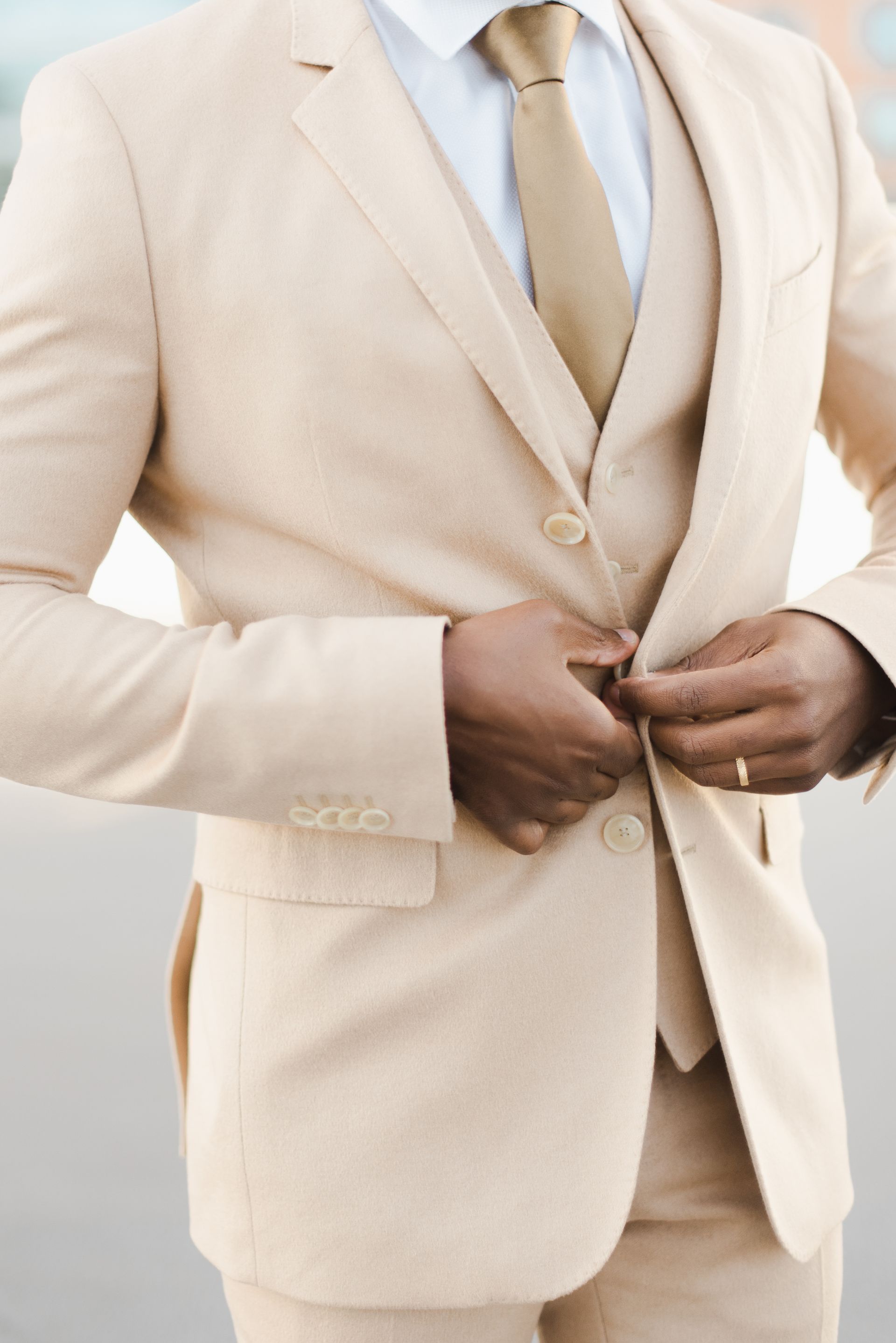Man in tan suit buttons his jacket.